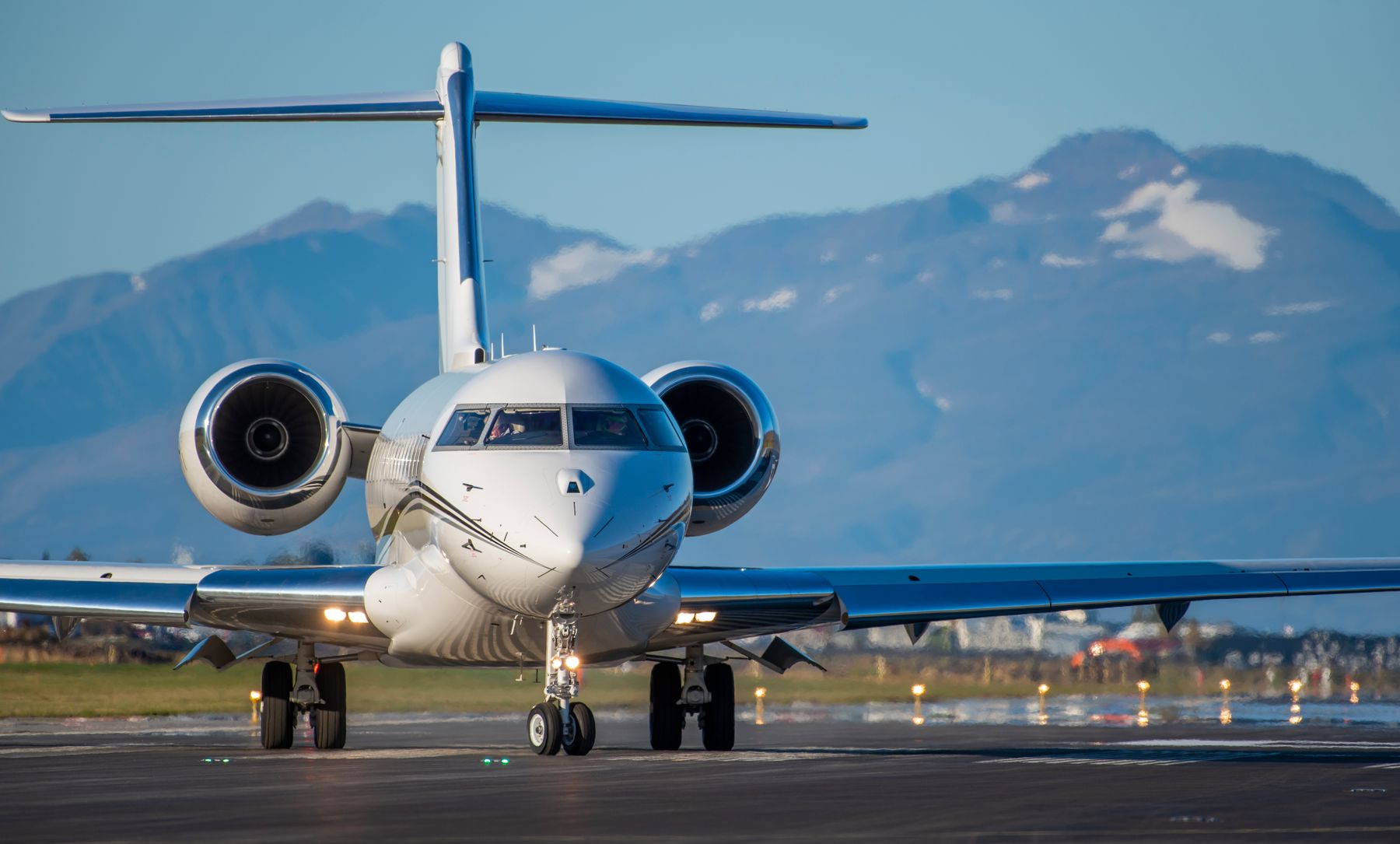 A white business jet on an airport runway with mountains in the distance
